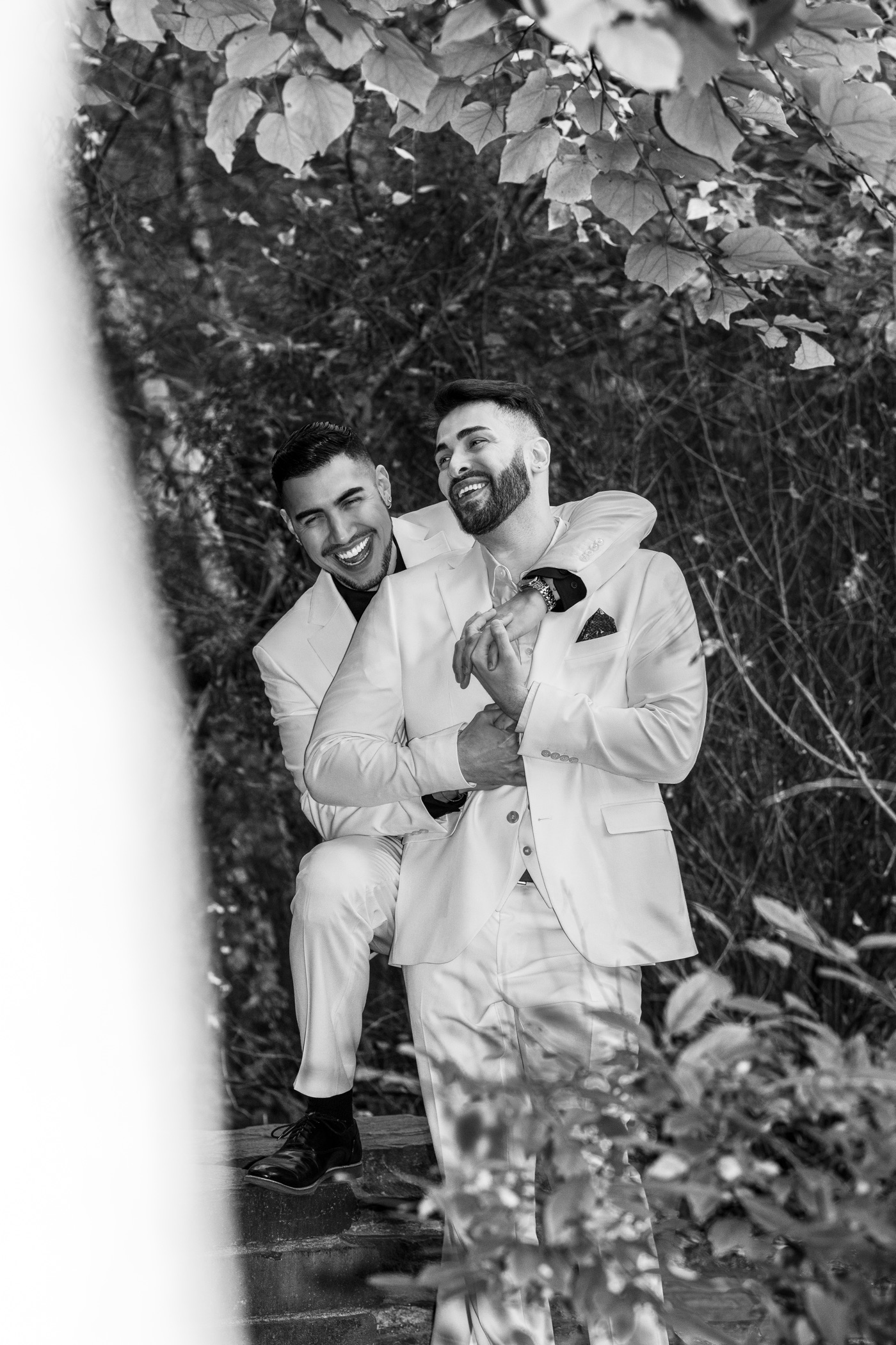 Two grooms laughing together in a black and white garden portrait