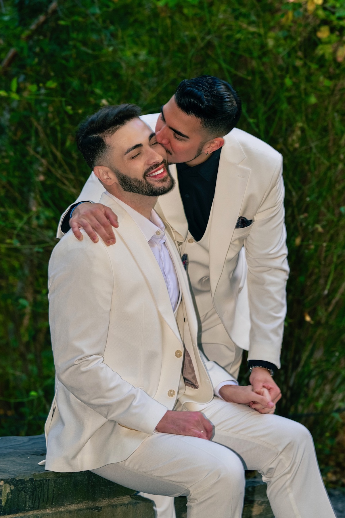 One groom kissing the other during a garden portrait