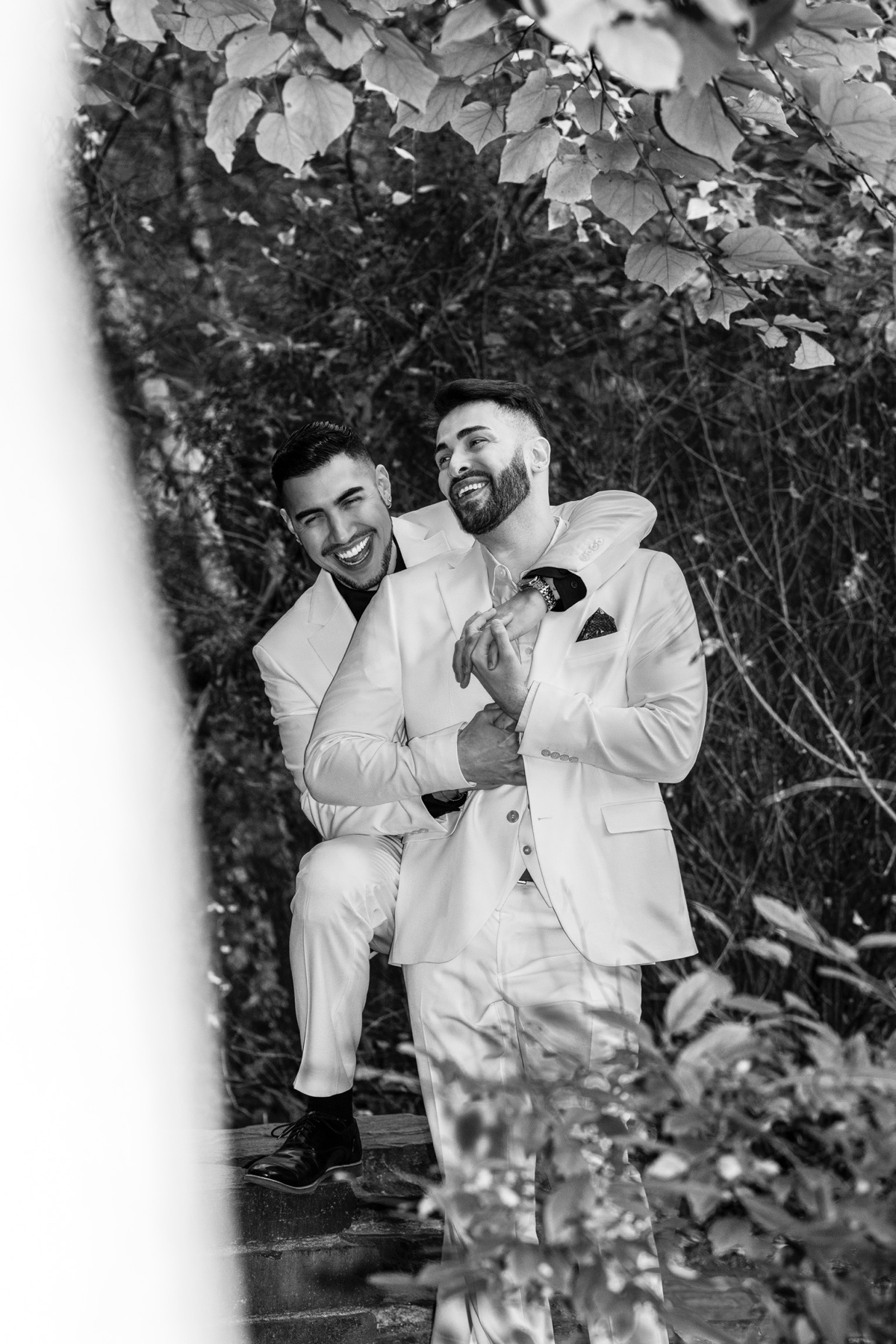Two grooms laughing together in a black and white garden portrait