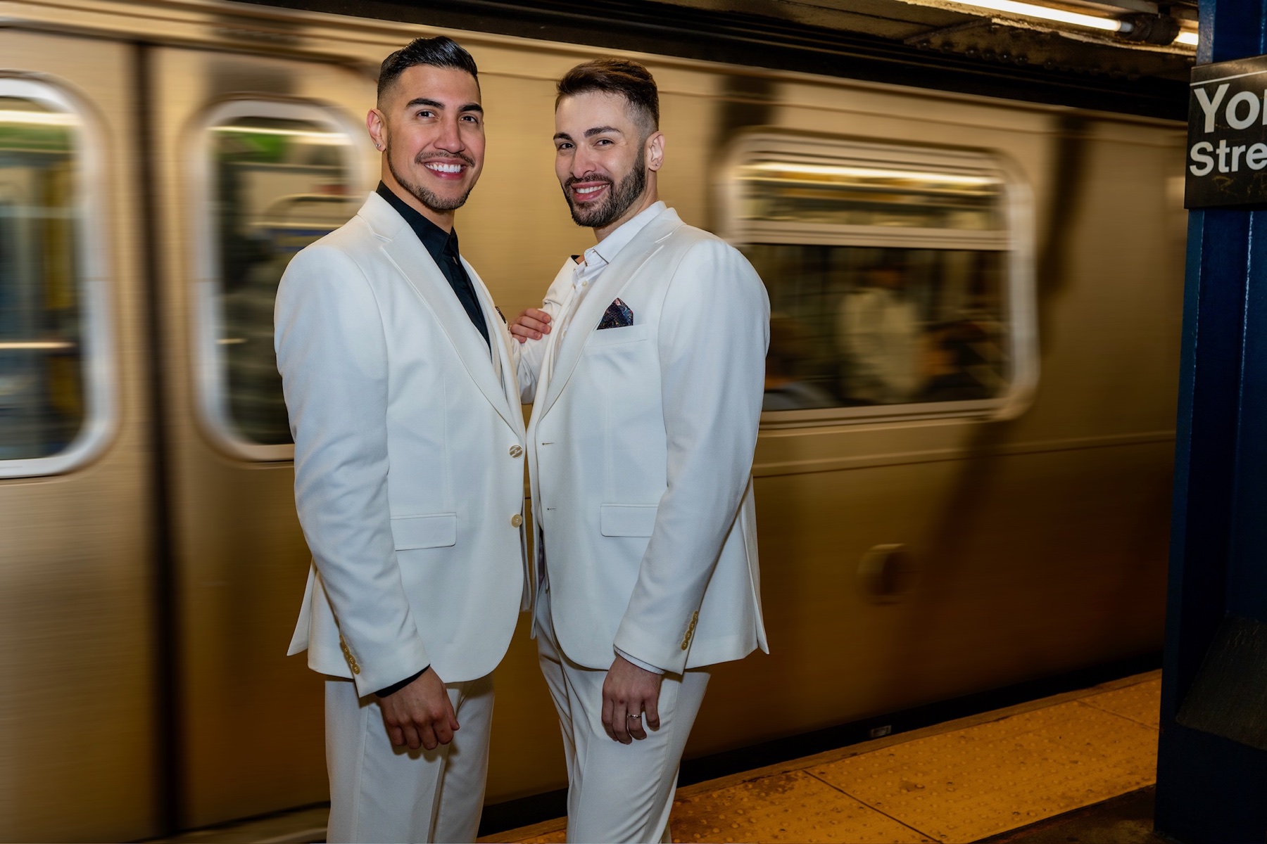 Two grooms in white suits standing on a subway platform