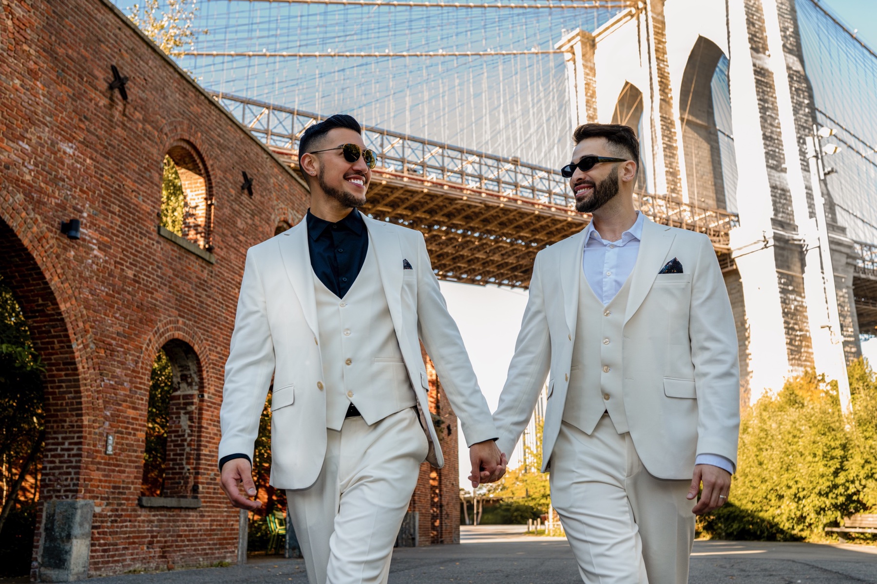 Two grooms walking hand in hand beneath the Manhattan Bridge